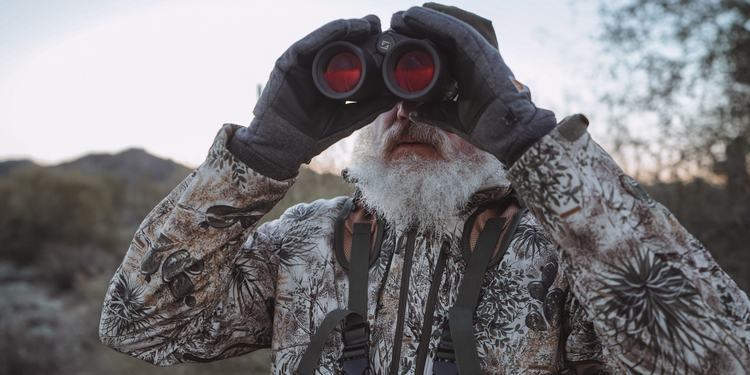 Man wearing GameGuard outerwear gear and holding binoculars