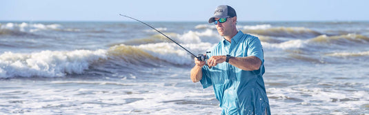 Man standing in ocean fishing wearing GmaeGuard MicroFiber Shirt and GameGuard cap
