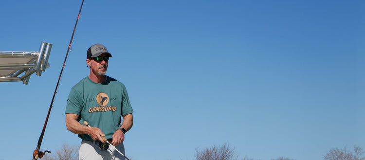 Picture of a man holding a fishing rod and wearing an Ironwood Graphic Tee, Tarpon Travel Shorts, and a GunMetal GameGuard Cap.