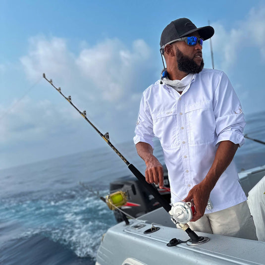 man doing some fishing off a boat wearing gameguard white long sleeve microfiber shirt and gameguard caviar cap and caviar meshback