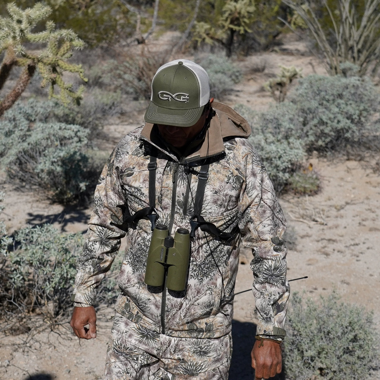 man walking wearing gameguard guia grande jacket and pants with olive cap and stone meshback