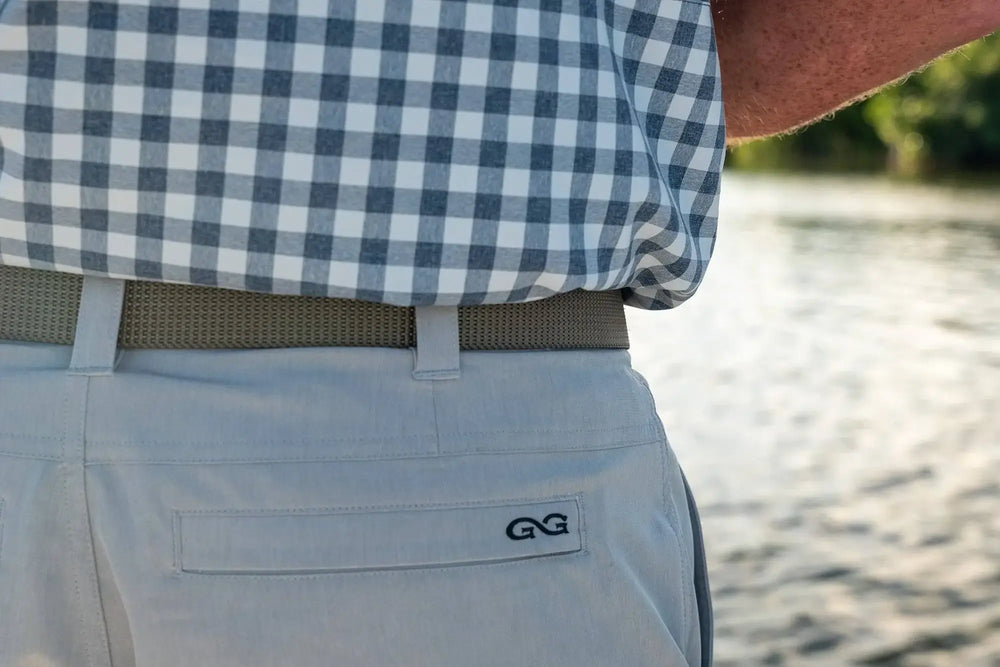 man wearing gameguard tarpon travel shorts and short sleeve glacier pearl snap shirt while standing on a boat floating on the water