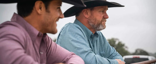 two men looking off in the distance wearing pearl snap shirts and cowboy hats. One is wearing a crimson red pearl snap and the other a deep water blue pearl snap